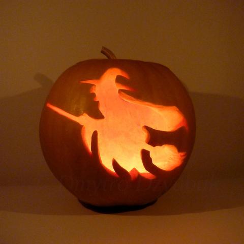 Witch wearing a black waving cloak and a pointed hat, flying on a broomstick is depicted on a carved pumpkin. Pumpkin with a candle inside.
