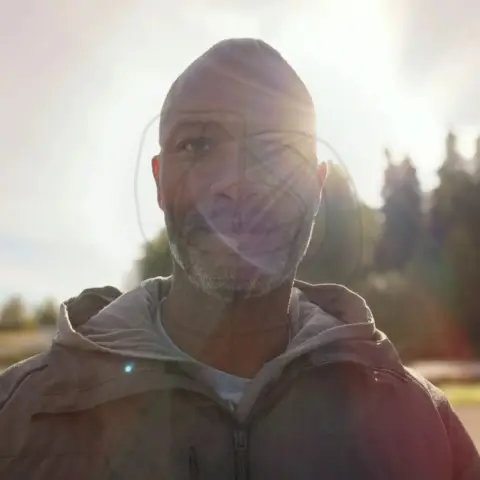 Headshot of Dane Broderick with protective code symbol overlay.