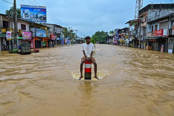 A man sits on a divider in the middle of a flooded road.