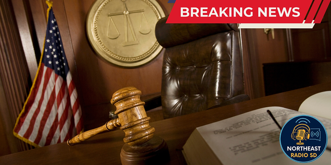 Gavel on desk, scales of justice emblem, U.S. flag in a courtroom. "BREAKING NEWS" and "NORTHEAST RADIO SD" visible, serious mood.
