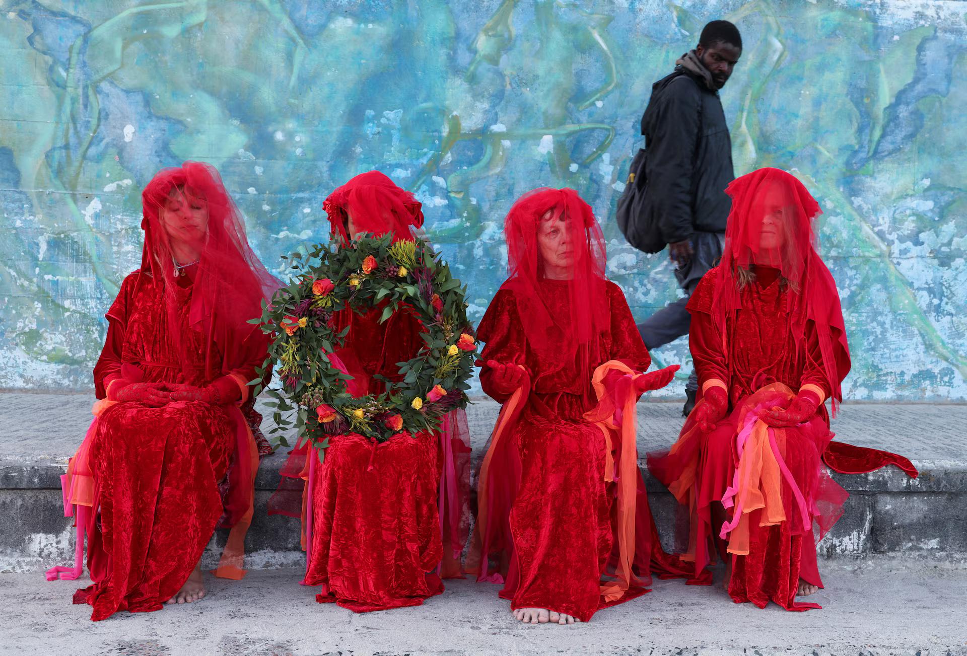 A man walks past members of Extinction Rebellion dressed in red during a wreath-laying ceremony marking Remembrance Day for Lost Species.
