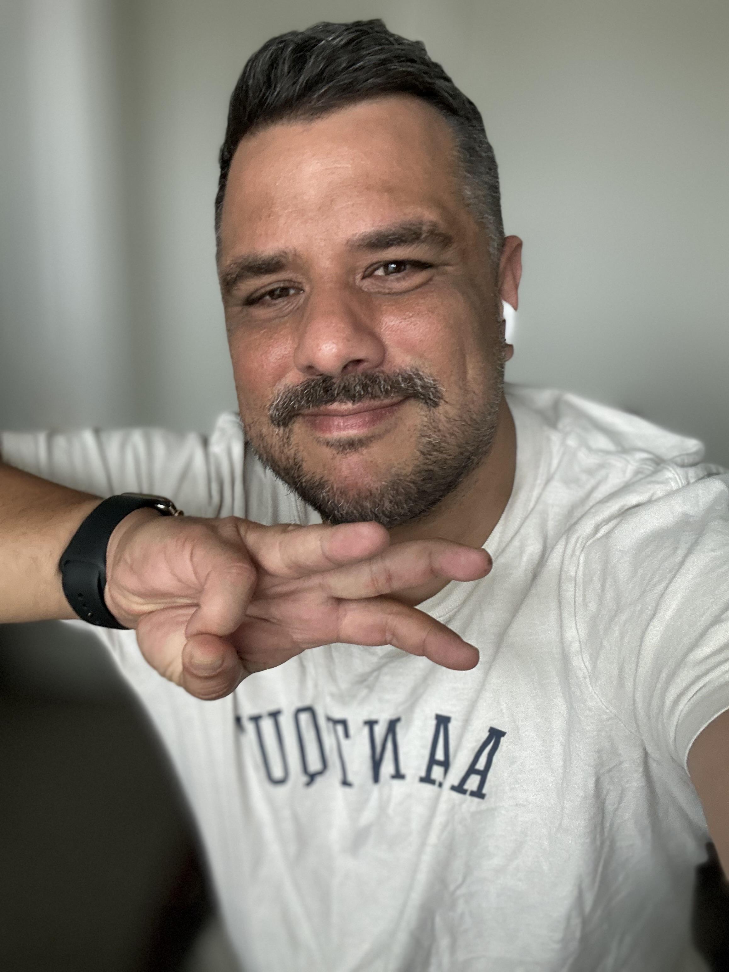 Me holding up three fingers. I'm in a white t-shirt with AirPods in. 