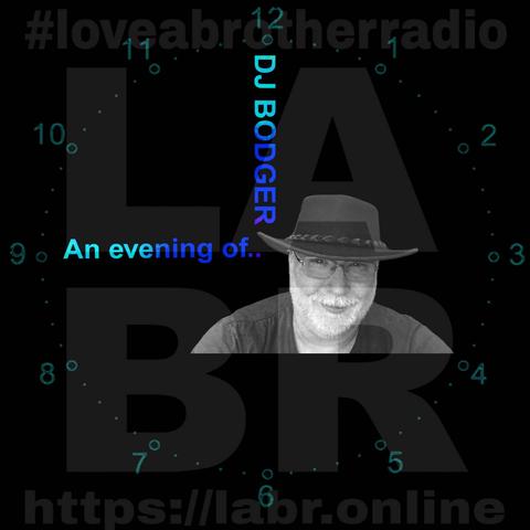 A dark image with #LoveABrotherRadio in dark grey at the top of the image. A large LABR fills the background of most of the image. The URL https://labr.online is at the bottom of the image. Around the outside are the numbers of a clock face with two clock hands pointing to 12 and 9 indicating 9 o'clock. The hand pointing at 9 reads "An evening of" and the hand pointing at 12 reads "DJ BODGER" In the lower right of the clock face is the image of DJ Bodger. He is a bearded man of late 40s wearing glasses and an Australian bush hat.