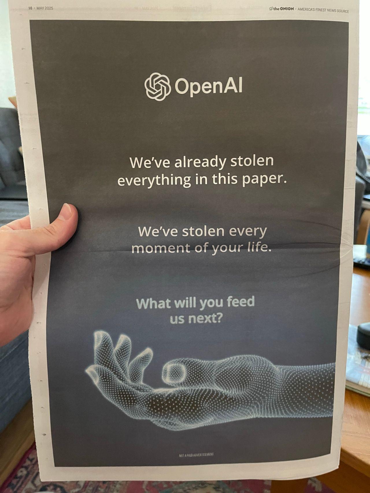 A photo of a full page printed newspaper (The Onion) featuring a full-page ad, dark background, sparse text:
OpenAI (logo)
We've already stolen everything in this paper.
We've stolen every moment of your life.
What will you feed us next?
in tiny text at the bottom: "not a paid advertisement"