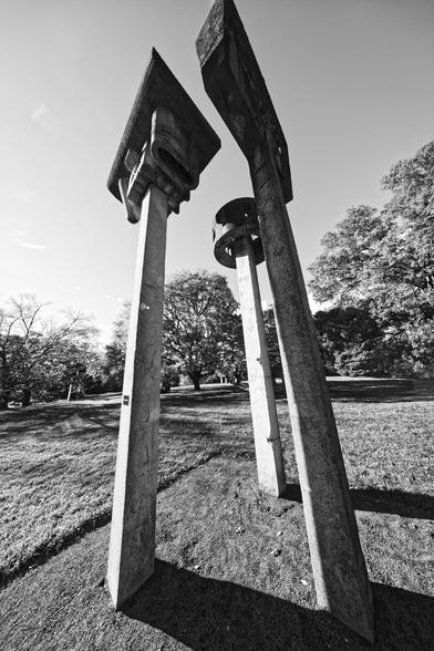 Three concrete poles with various shapes on top surrounded by close cropped grass and further away trees