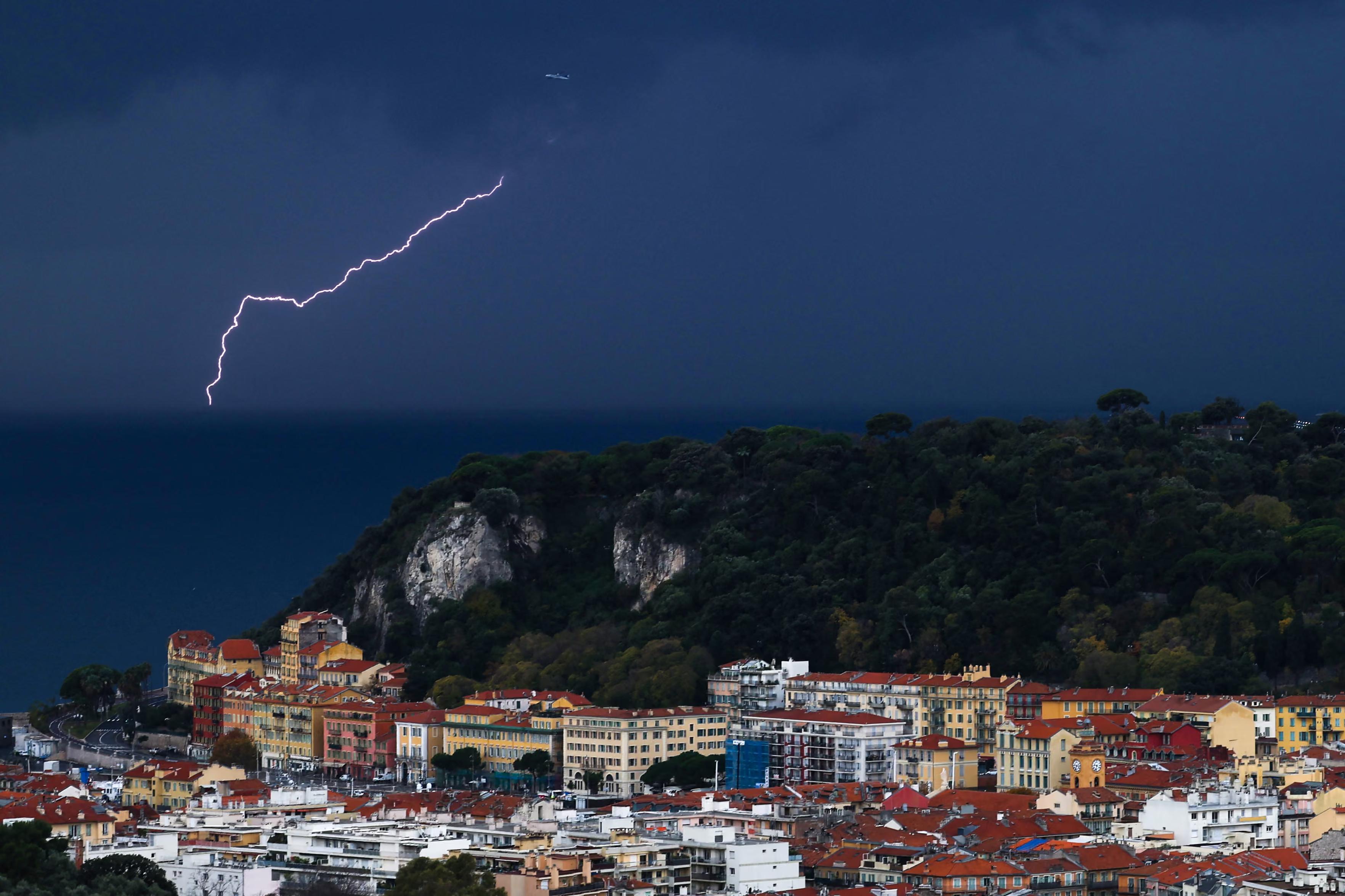 Lightning forks to the horizon as a jumbo jet departs from the Mediterranean coast.