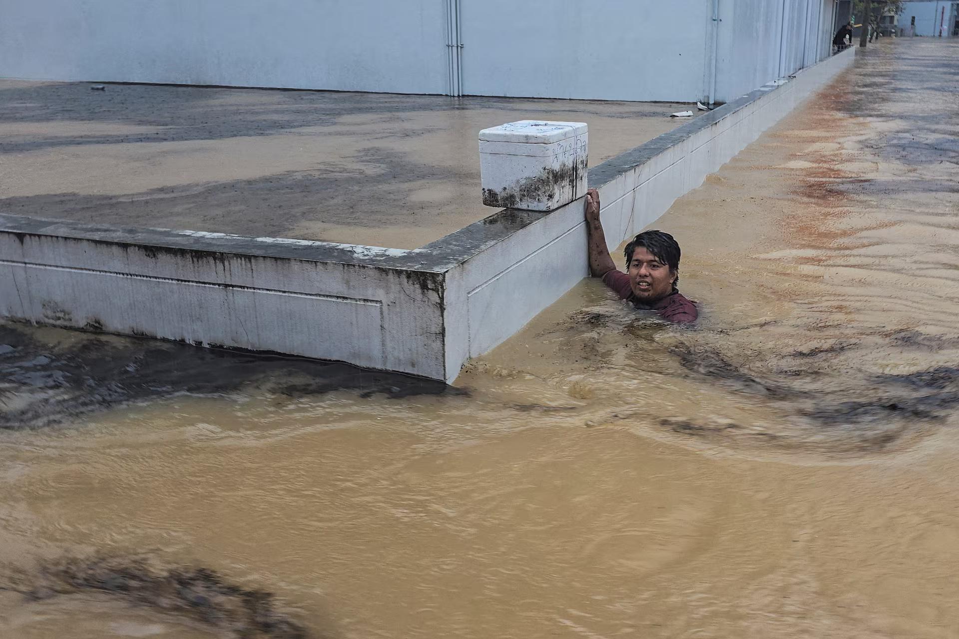 A man clings to a wall in a flooded street.