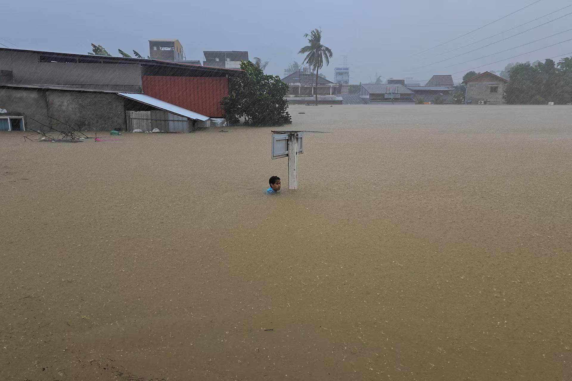 A man clings to a street sign pole in a flooded street after being swept by the water.