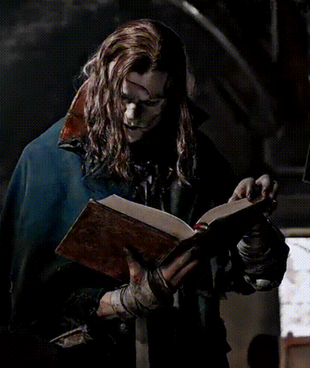 Jacob Elordi as Frankenstein's creature, standing and leafing through pages of a large book, with a curious, interested facial expression.