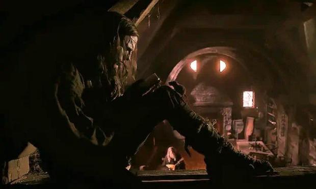 Jacob Elordi as Frankenstein's creature, sitting comfortable on the woodwork under the roof of a house, reading.
