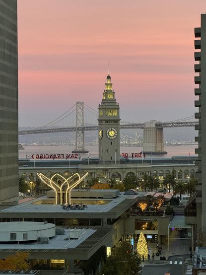 San Francisco looking east from the Financial District at the Ferry Building, Bay Bridge, and bay with a pink sky.