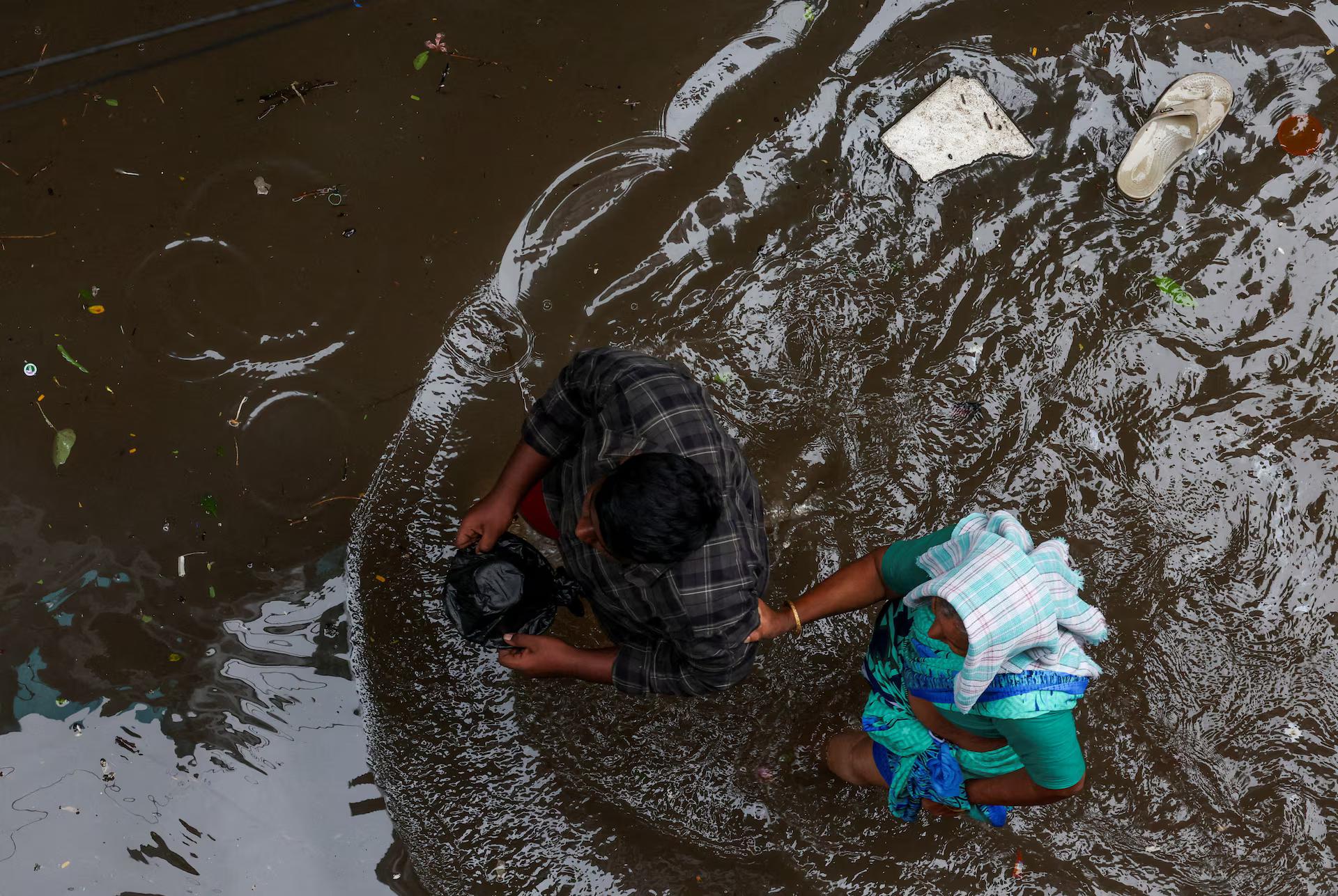 A woman holds a man's hand as they wade through a waterlogged street.