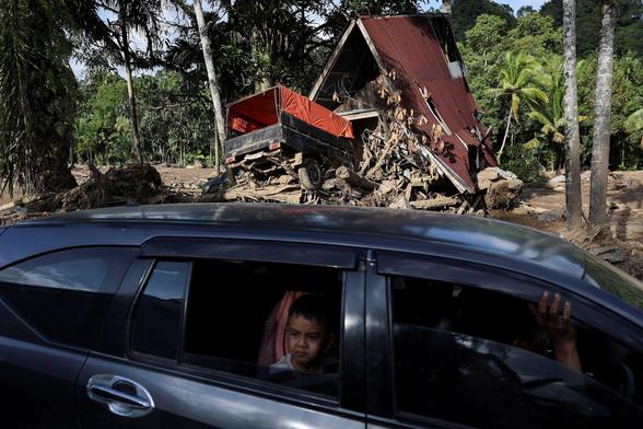 A boy looks from a car at an area hit by deadly flash floods (a truck carried by flood into a house).