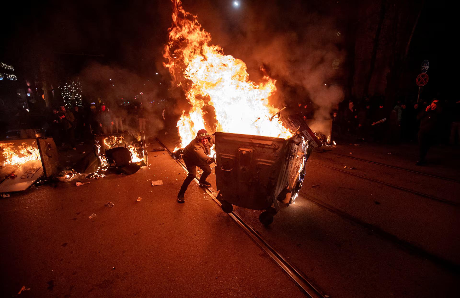A protester pushes a burning garbage bin during scuffles with police.