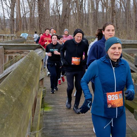 Runners dressed for the cold crowd across a wood bridge