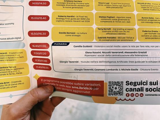 A photo of a hand holding up a brochure… next to 17:00 there is the description: “Elena Rossini, Niccolò Venerandi, Alessandro Grazioli - Ripensare i social: dalla centralizzazione alla federazione” “