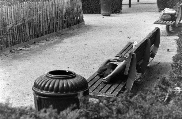 dans un parc, un homme dort allongé sur un banc, en noir et blanc
