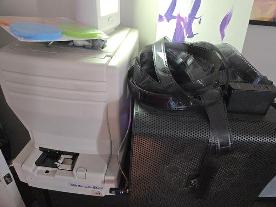 An image of a pile of film on top of a cube-shaped computer, itself next to a Noritsu LS-600 film scanner.
