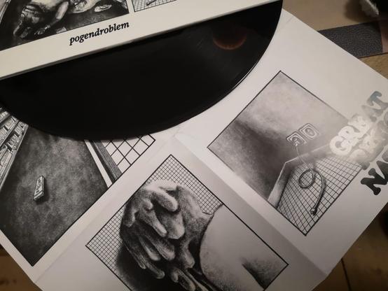 Ein Bild einer schwarzen Vinylplatte, die teilweise von einem illustrierten Albumcover verdeckt ist. Das Cover enthält Schwarz-Weiß-Illustrationen mit verschiedenen Skizzen, darunter eine Figur auf dem Boden, eine gefaltete Hand und eine Steckdose mit Kabel. 