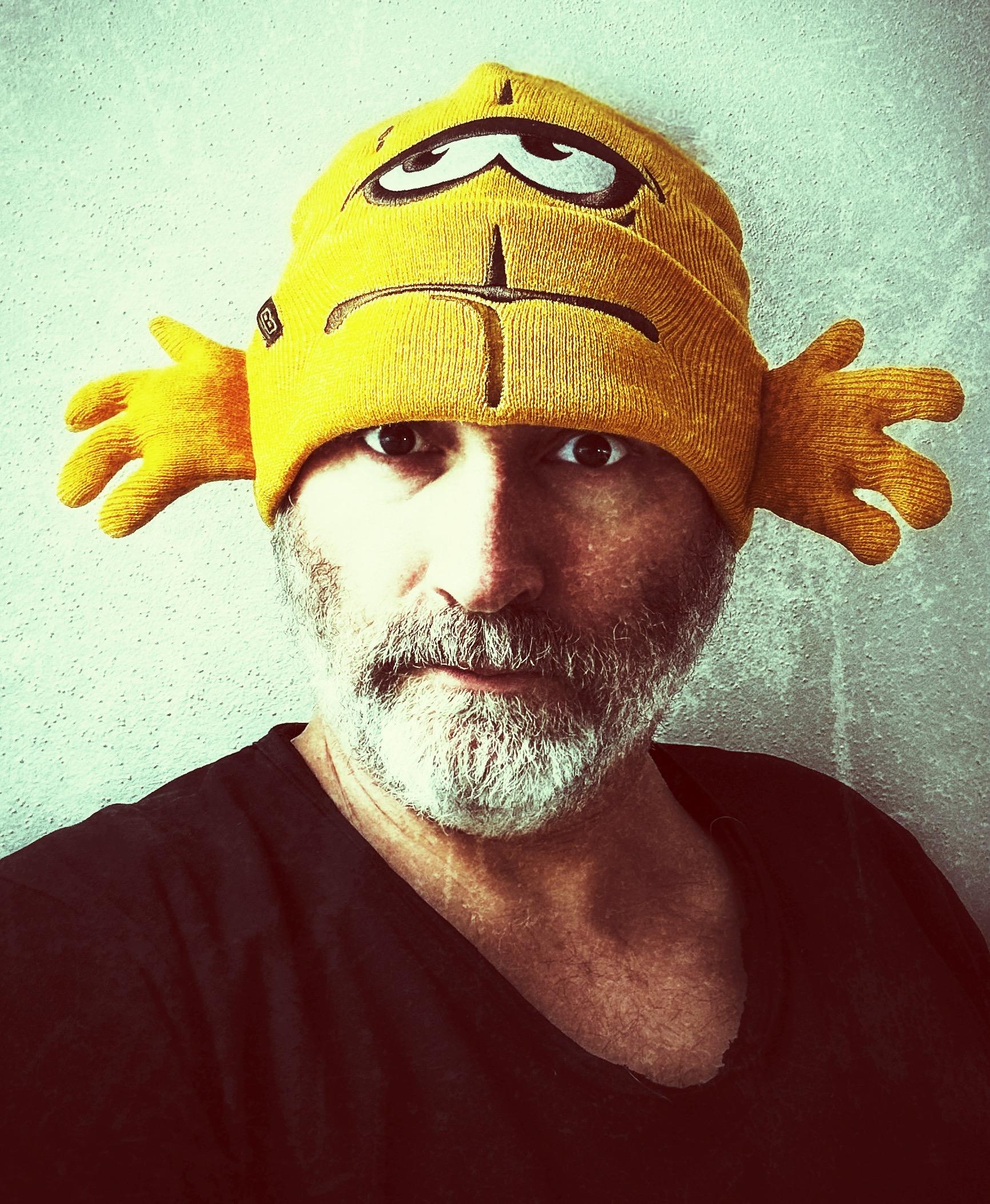 Ein Selfie im vintage Look mit Kratzern und Überbelichtung: Ich blicke ernst in die Kamera und trage eine Bernd das Brot Bütze auf dem Kopf. Die Mütze sieht aus wie die "obere Hälfte" von Bernd das Brot, also mit Mund und Augen. Links und rechts sind Hände angenäht. Es sieht also aus, als trüge ich Bernd auf dem Kopf. 