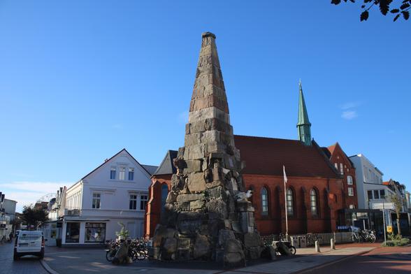 Ein 13m hoher Obelisk aus unterschiedlichen Steinen zusammengesetzt. Auf einem Sockel steht eine weiß-graue Möwe mit ausgebreiteten Flügeln.
Das Denkmal befindet sich auf einem kleinen Platz, eher einem Straßeneck, mit einer Kirche dahinter.