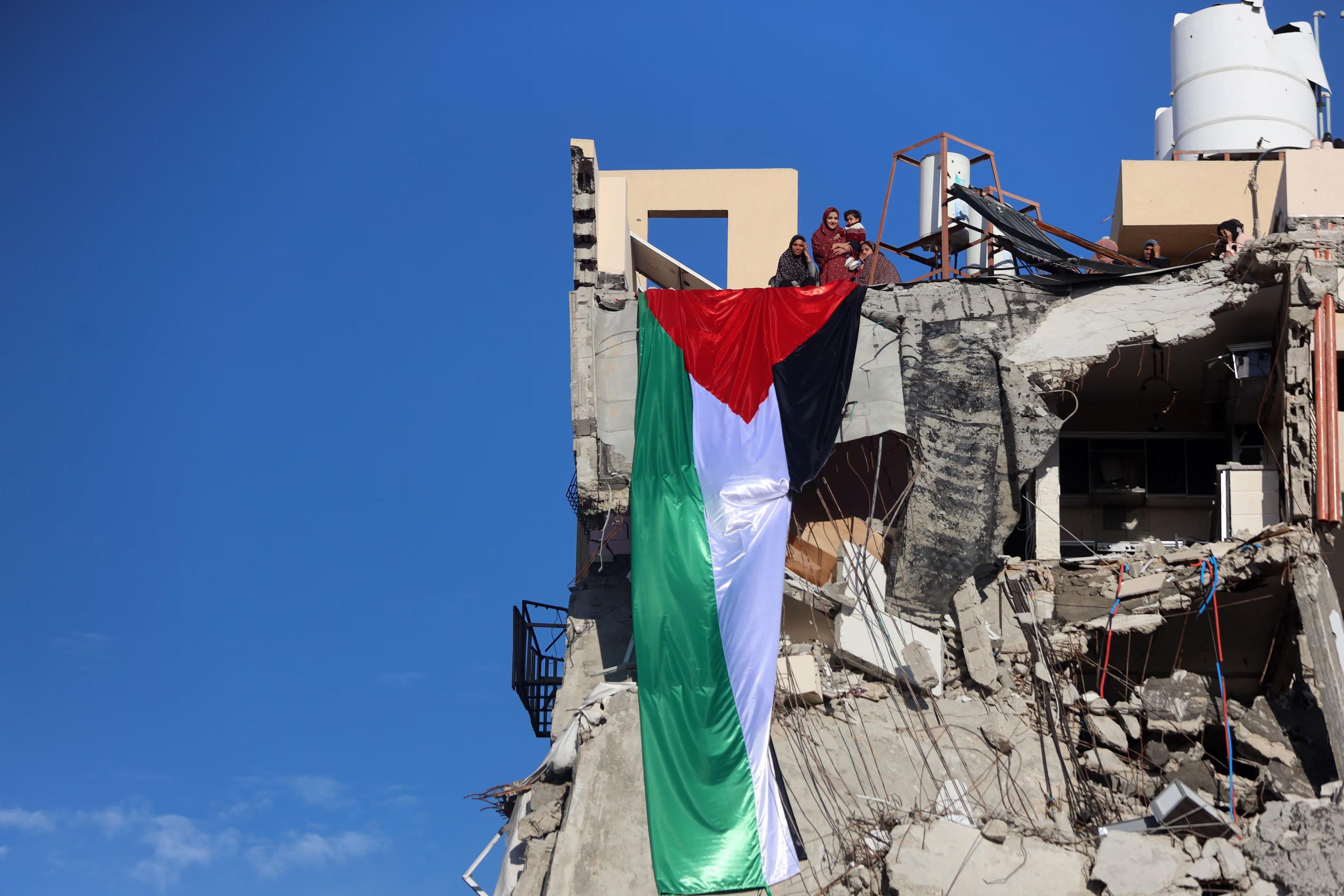 A huge Palestinian flag hangs as women watch from the top of a building destroyed during the Gaza war.
