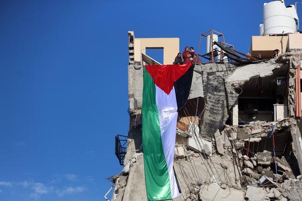 A huge Palestinian flag hangs as women watch from the top of a building destroyed during the Gaza war.
