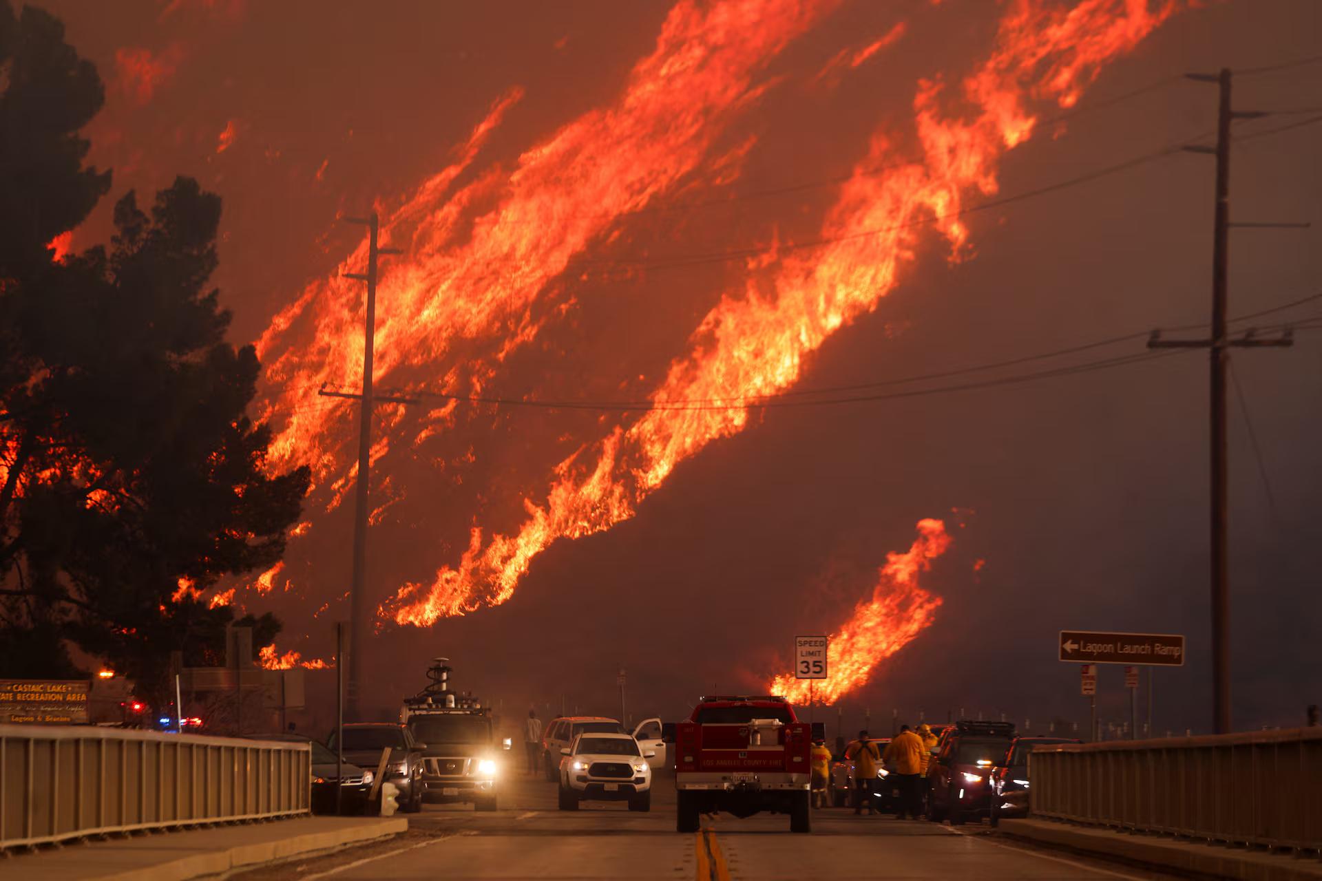 Flames rise behind vehicles as the Hughes Fire burns in Castaic Lake, California,