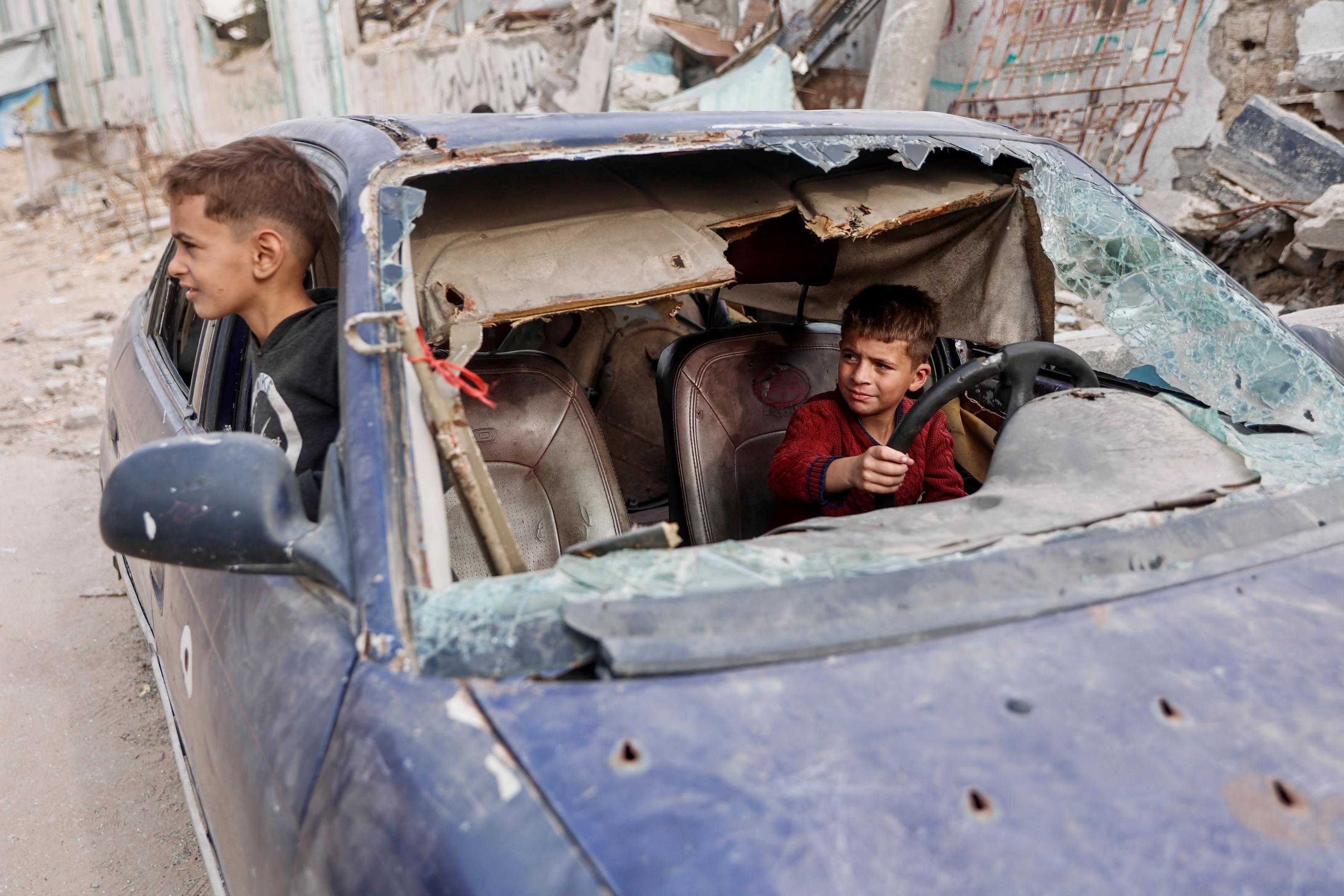 Displaced Palestinian children play in the wreckage of a car.