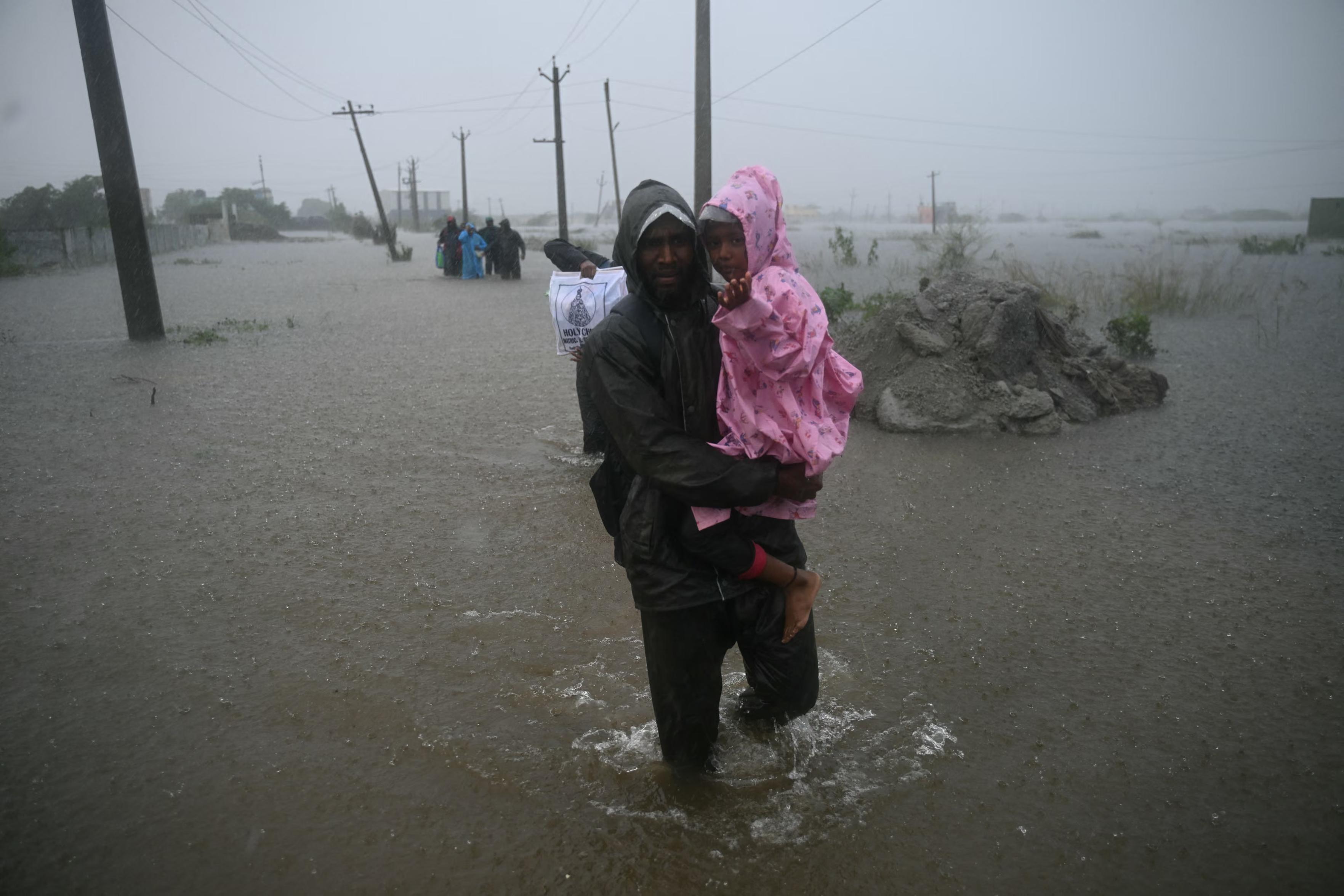 A man carrying a child in pink raincoat in flood waters.
