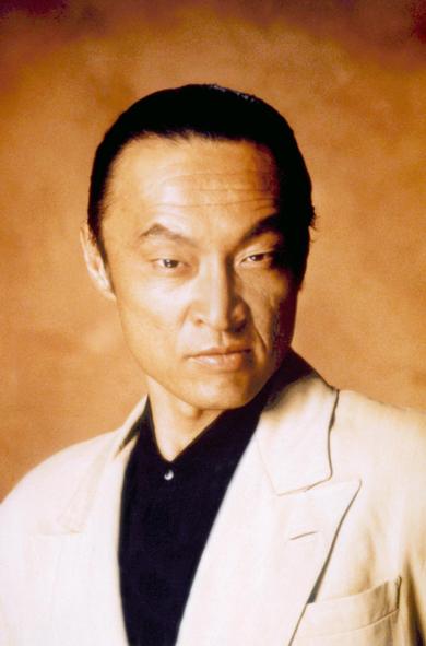 Japanese-born actor and film producer Cary-Hiroyuki Tagawa as leader of The Iron Claw gang, Funekei Yoshida in the 1991 American buddy cop action film “Showdown in Little Tokyo” . He’s wearing a pale colored suit with a black shirt and looking menacingly at the camera.