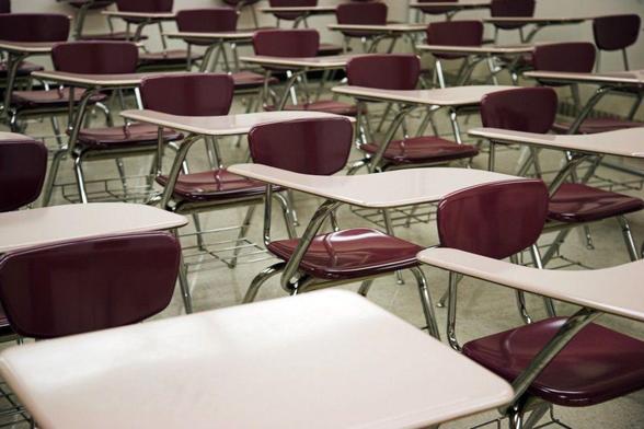 A photograph of a mass of carefully aligned red classroom chairs with built-in writing surfaces, all facing forward. Image attribution: Flickr user dcjohn