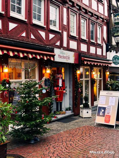 Festlich geschmücktes MärchenCafé in der Altstadt von Grünberg. Vor einem rot-weißen Fachwerkhaus stehen ein großer Nussknacker, ein Weihnachtsbaum und weihnachtliche Dekorationen. Warmes Licht fällt auf das Kopfsteinpflaster und erzeugt eine märchenhafte Adventsstimmung.