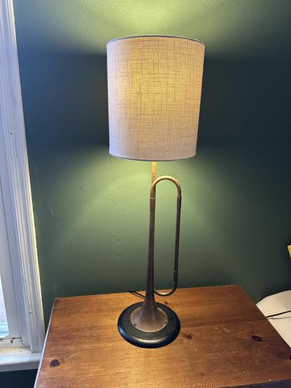 Table lamp made of a horn with patina. White lampshade and black base on a wooden surface in a green painted room.