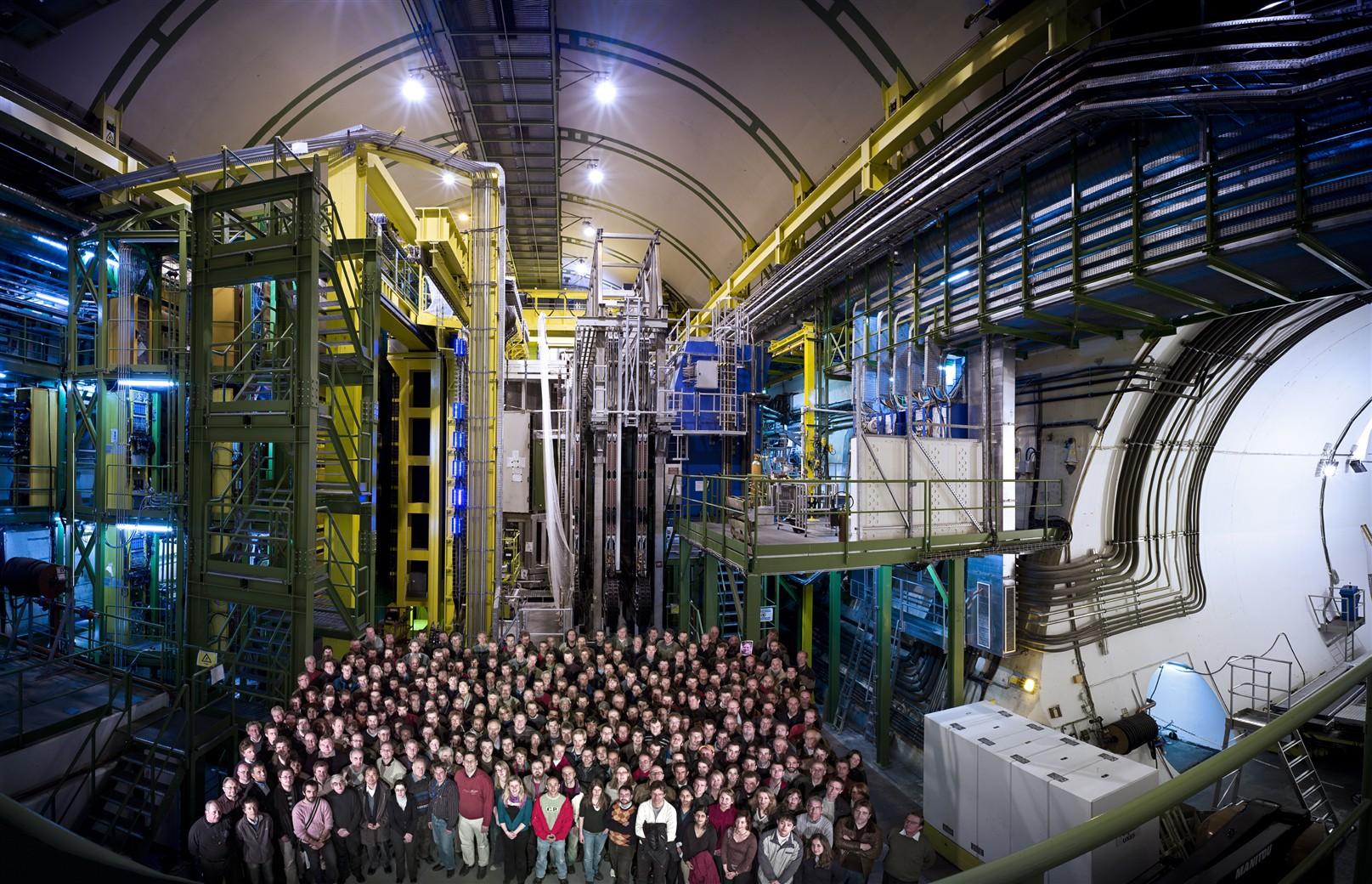 View of the LHCb detector hall, and its immense scale, relative to hundreds of collaboration members shown standing on the floor beneath the detector apparatus.