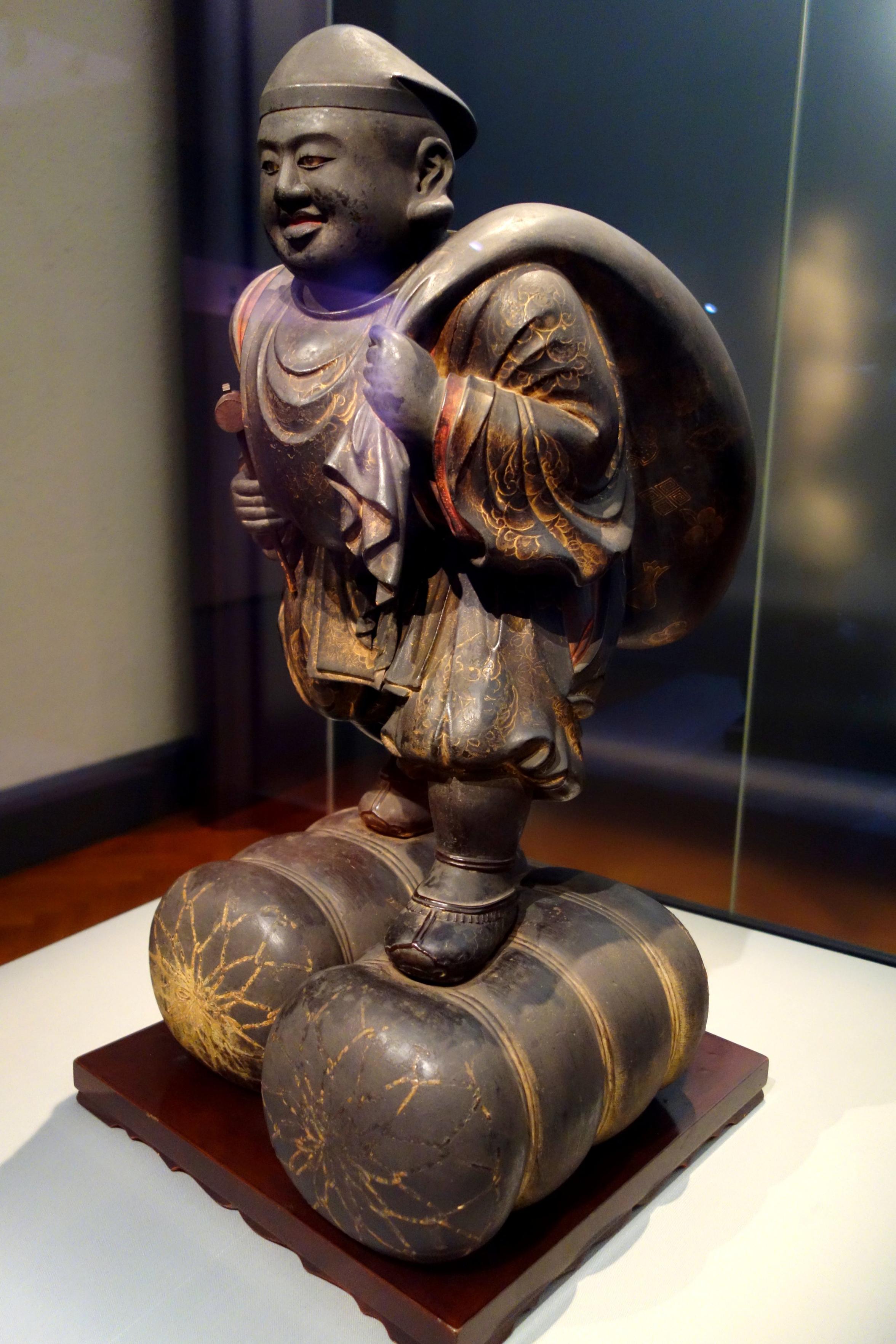 Statue of Daikokuten in his usual pose, standing on rice bales with a sack slung over his shoulder.