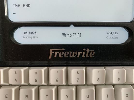 A detail of my Freewrite Smart Typewriter, including the status screen showing 87,108 words written on my new first draft. The portion of the screen shown above it displays the words THE END.