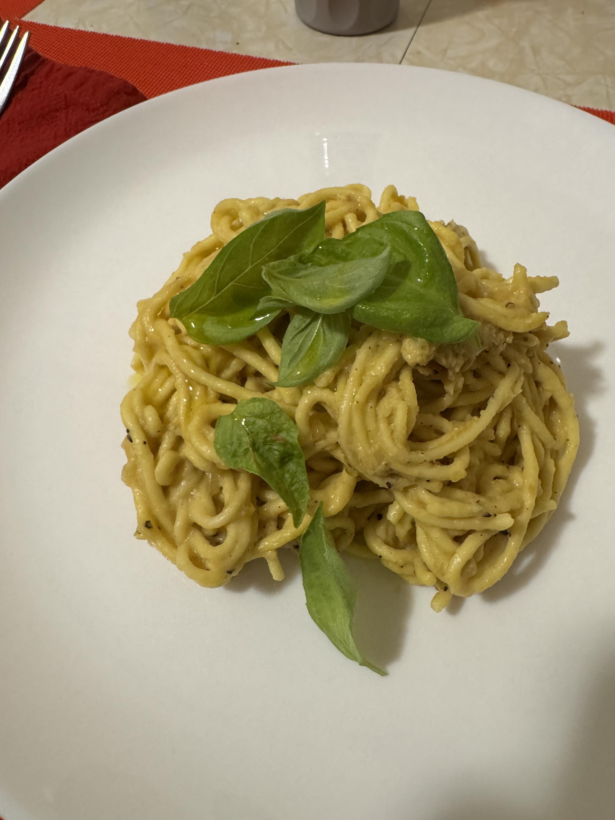 A birds nest of pasta sits on a whole plate. It’s got a clingy yellow sauce. There are a few basil leaves scattered on top.