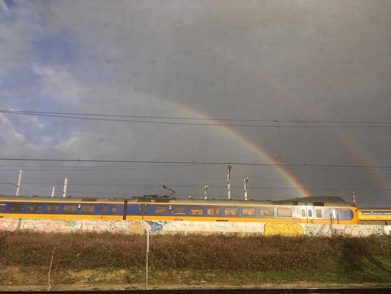 Koploper-treinstel, met dubbele regenboog tegen een halfbewolkte lucht