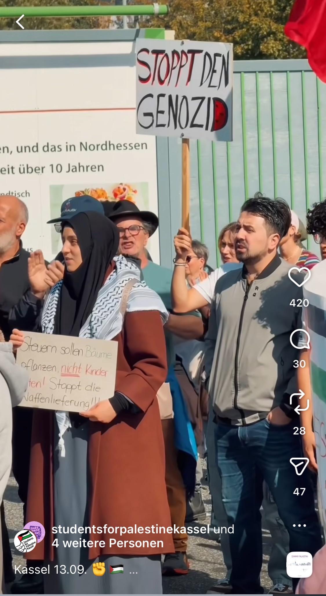 Eine Gruppe von Menschen nimmt an einem Protest teil. Es werden Schilder gehalten, darunter eines mit der Aufschrift "STOPPT DEN GENOZID".