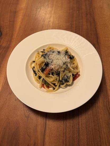 Ein tiefer Teller Linguine, tief dunkelgrüne Blätter von Schwarzkohl, kleine rote Stücke von frischer Tomate, darüber grob geriebener Parmigiano Reggiano.