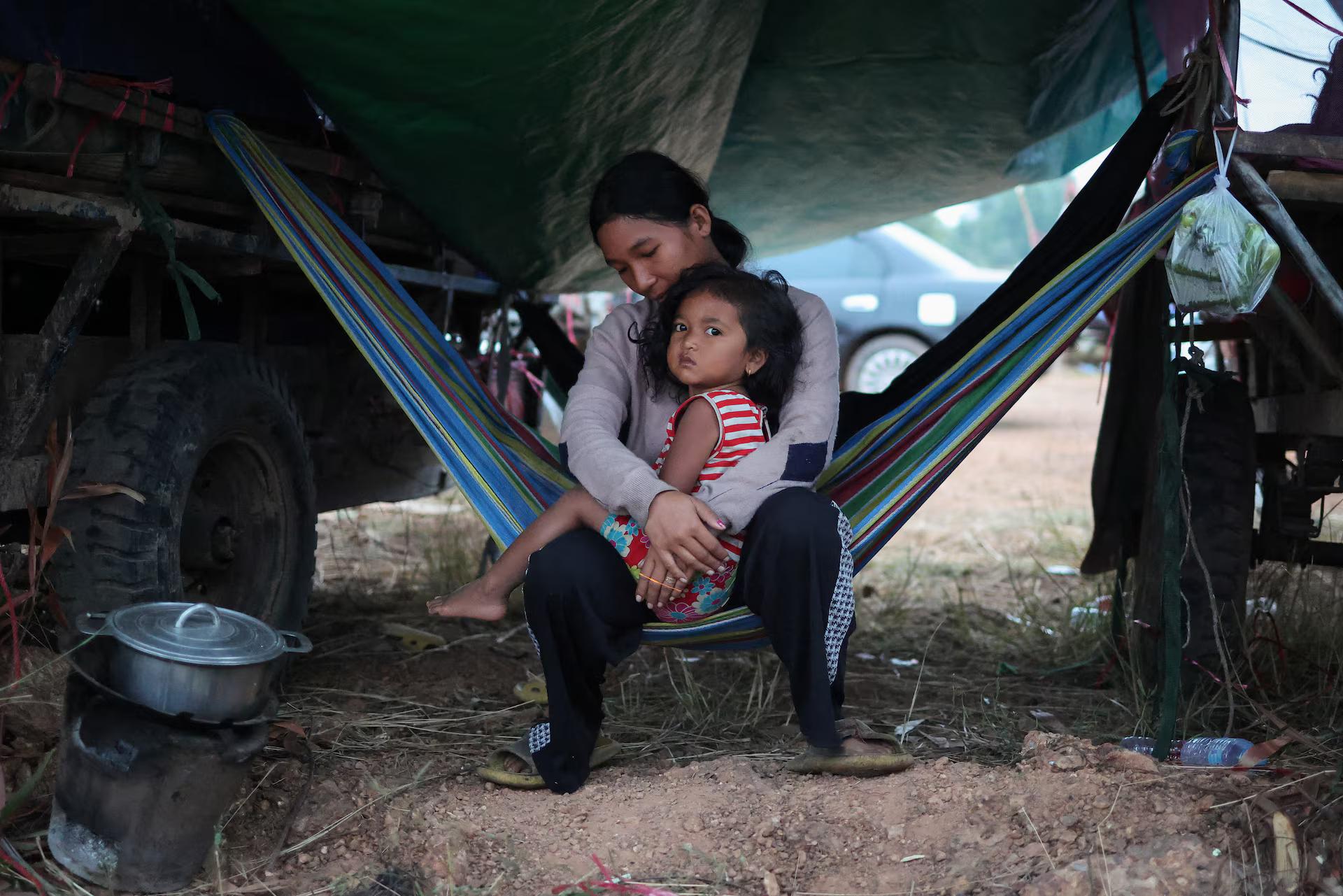 A woman with a child sits on a hammock in a tent.