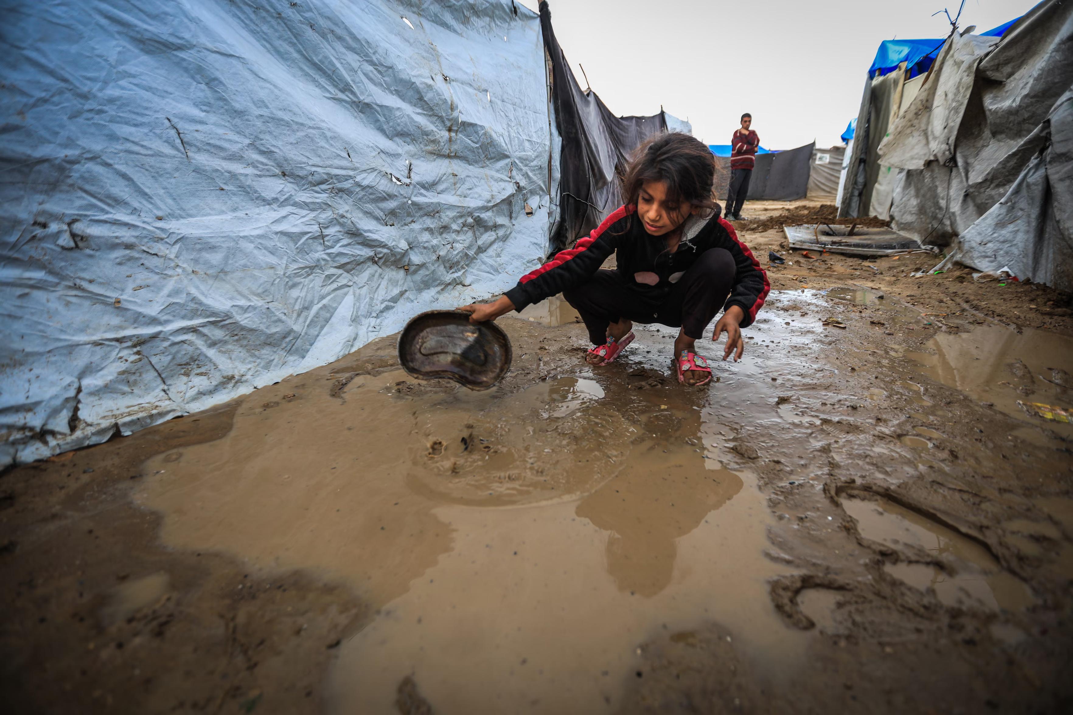 A girl scoops up water from around her family tent.