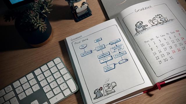 Open notebook showing a hand-drawn module diagram and December calendar, beside a keyboard and succulent on a wooden desk.