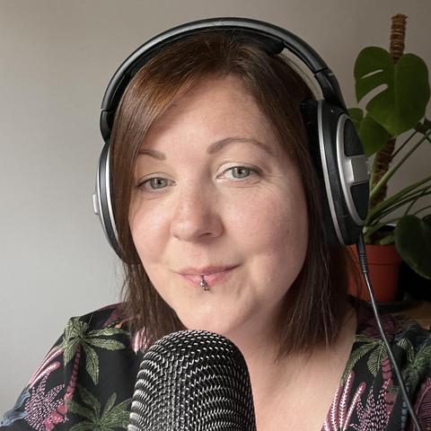 A photo of Claire (Robot Talk host) looking happy. She's wearing headphones, there's a microphone in front of her and a monstera plant in the background.