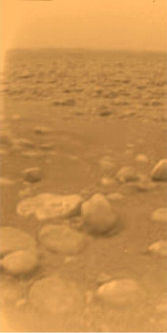 Narrow picture taken by the Huygens probe from the surface of Saturn's moon, Titan, revealing a yellow atmosphere and surface covered in rocks and boulders.