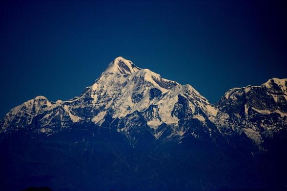 Photograph of Trishul I, II, and III in the Kumaon Himalayas, seen here from the south-west, showing its huge ice-covered flank and three stepped summits against a deep blue sky. (To the left is Nanda Ghunti, and to the right is Mrigthuni, neither peak seen completely here.)