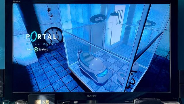 A television displaying the title screen for the game Portal. A handful of knickknacks can be seen along the bottom bezel.  