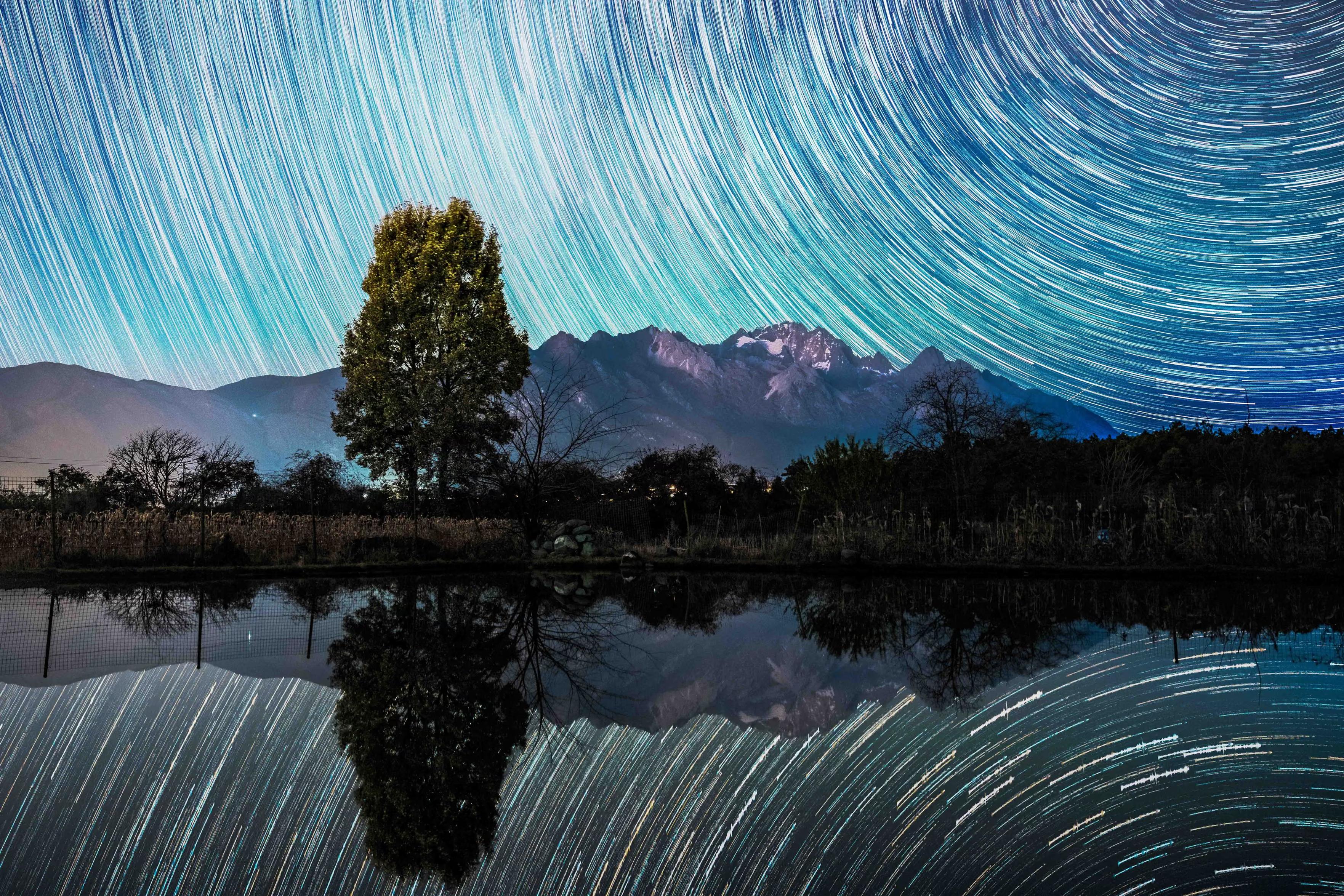 A stack composite photo shows the starry sky during the Geminid meteor shower reflected in water.