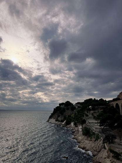 Mittelmeerküste bei Marseille mit bewaldeter Klippe und dramatischen Wolken über dem Meer
